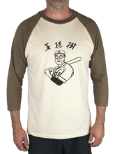 Front view of man wearing a Kaoru Betto baseball shirt, with olive green raglan sleeves, a beige body, and a black screenprint of a Japanese baseball player